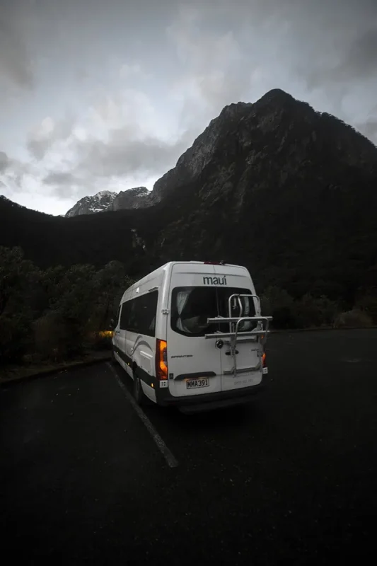 Milford Sound Swing: Where To Find It (2025) 12 Our white Maui campervan with a bike rack is parked near the forest in the Milford Sound area, just before sunset.