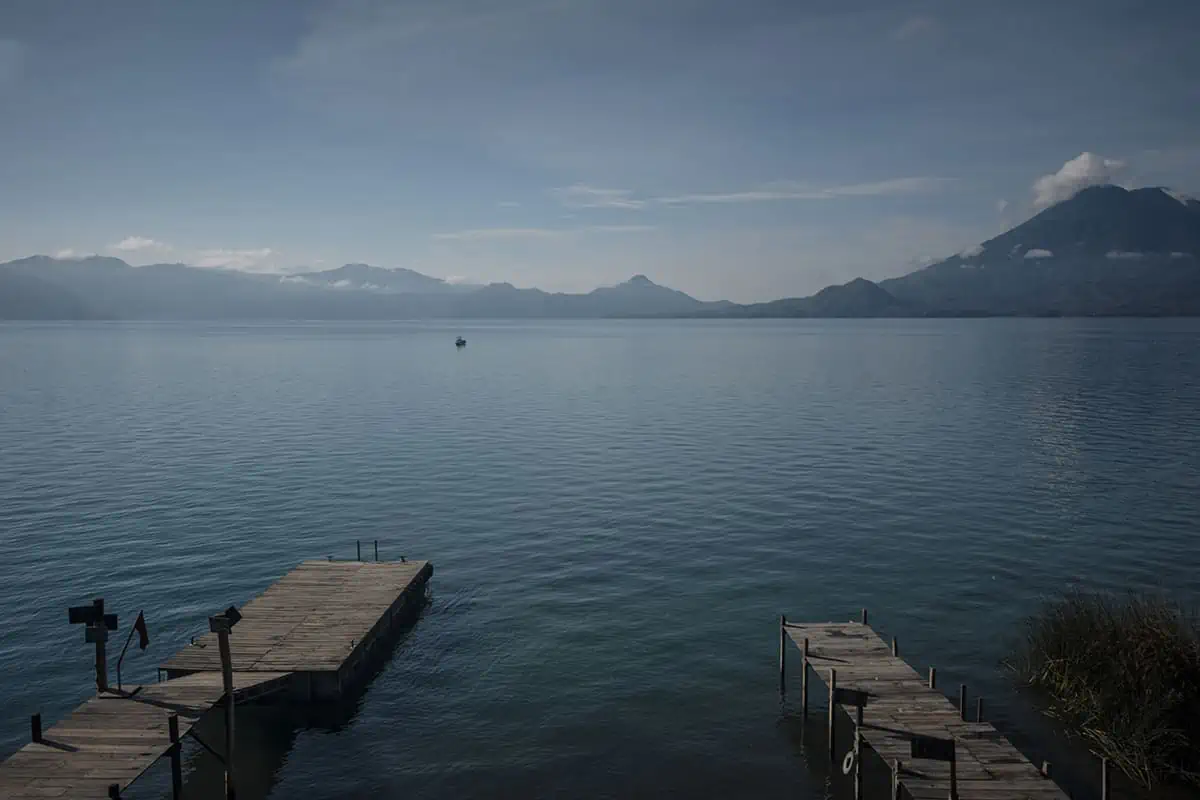 Panajachel To San Pedro & The Towns Between: How To Travel Around Lake Atitlan 46 looking out over two piers to the incredible volcanos and a lancha transporting passengers around lake atitlan