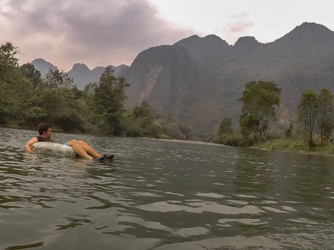Tubing In Vang Vieng, Laos: ULTIMATE GUIDE 2025 4 Tubing in Laos depicted by a man reclining in a tube on a river, surrounded by majestic mountains and a peaceful natural environment.