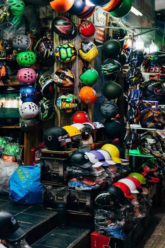 Scams In Vietnam: READ BEFORE YOU VISIT (2025) 5 A helmet shop in Vietnam displays rows of colorful helmets, some of questionable quality, piled and hung across every inch of the tiny space.