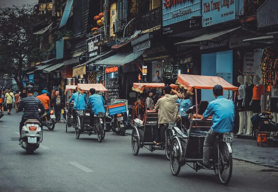 Scams In Vietnam: READ BEFORE YOU VISIT (2025) 14 A busy Vietnamese street filled with cyclos and scooters, as drivers in blue shirts transport tourists, unknown that they may be getting scammed.