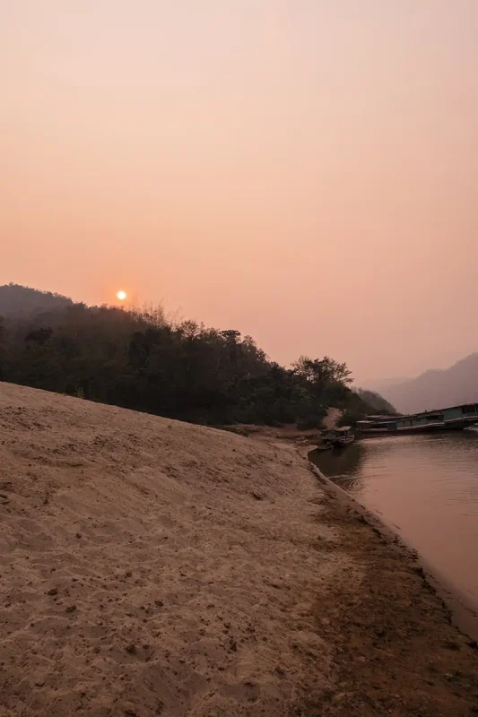 Taking The Slow Boat To Luang Prabang: BEST Tips 2025 14 The golden hour illuminates the serene Mekong River beside a sandy bank