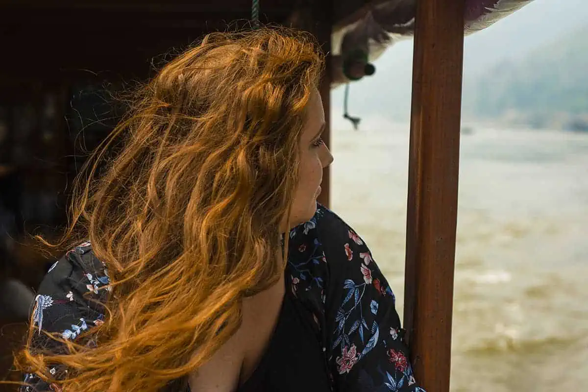 Taking The Slow Boat To Luang Prabang: BEST Tips 2025 23 tasha amy with flowing red hair gazes out from the shelter of a slow boat