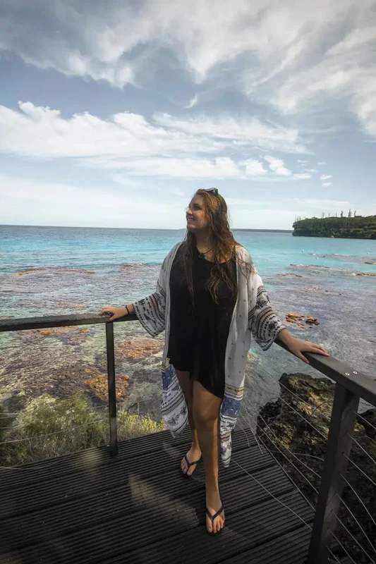 14 BEST Things To Do In Lifou: Cruise Passengers & More 24 tasha amy A happy woman leaning on a railing with a stunning ocean view, embodying the relaxed island lifestyle and the scenic beauty to enjoy in Lifou, New Caledonia.