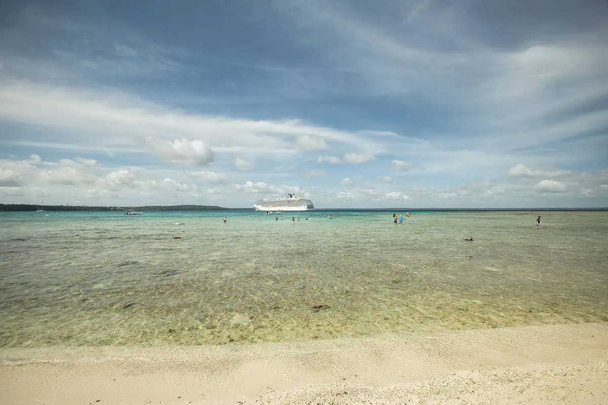 14 BEST Things To Do In Lifou: Cruise Passengers & More 27 A shallow, clear blue sea with people snorkeling and a cruise ship anchored in the distance, representing activities to enjoy when visiting Lifou from a cruise ship.