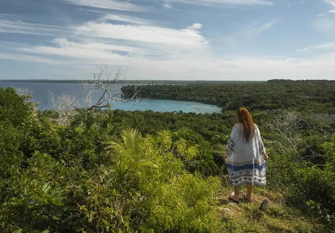 14 BEST Things To Do In Lifou: Cruise Passengers & More 2 A person standing at the edge of a lush overlook, gazing out at a secluded bay in Lifou, New Caledonia, showcasing one of the serene things to do in Lifou.