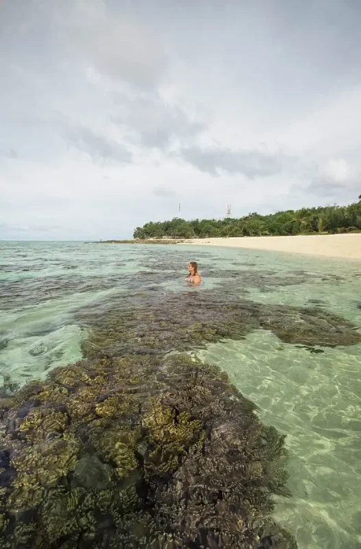 Things To Do On Mystery Island In Vanuatu: For Cruise Passengers & More 11 tasha amy stands waist-deep in the clear lagoon of Mystery Island, surrounded by coral heads and facing a peaceful, undeveloped beach with forested hills beyond.