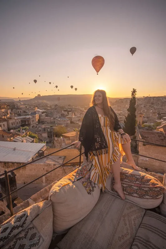 22+ Cheapest Countries To Backpack In The World! (2025) 36 tasha amy sits on a bed with pillows and hot air balloons in the sky.