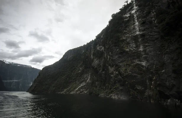 A part of the four sisters waterfall cascades down a steep cliffside into the still water, one of the best waterfalls in milford sound