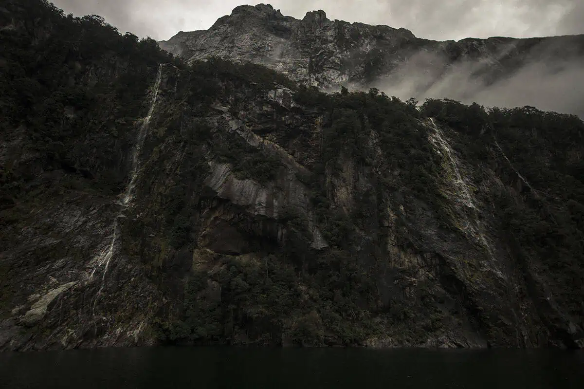 Best Waterfalls In Milford Sound Worth Checking Out 11 multiple waterfalls at four sisters falls descend from the mountain under a cloudy sky in Milford Sound
