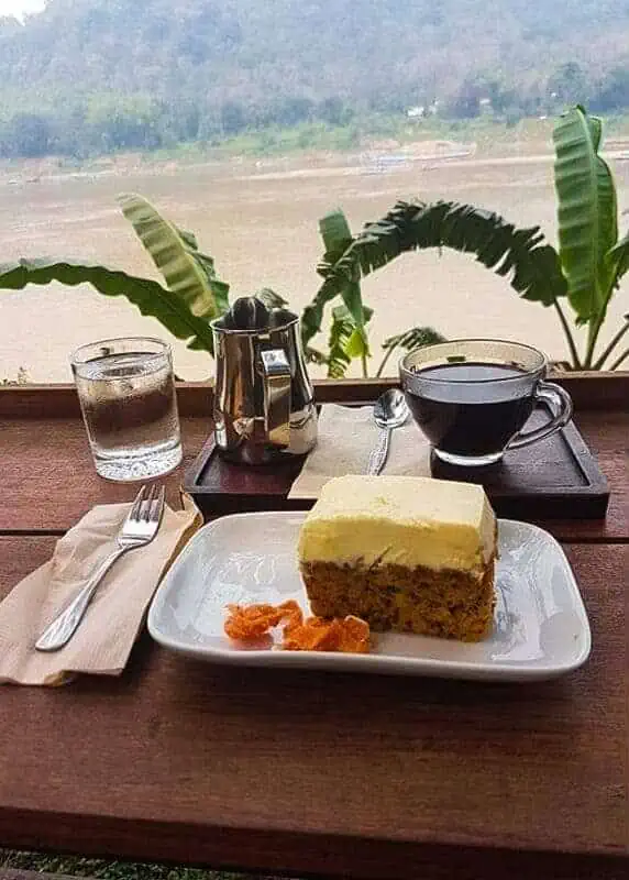 Where To Eat In Luang Prabang: 12 BEST Restaurants 2025 8 a slice of carrot cake and coffee looking over the river at saffron coffee