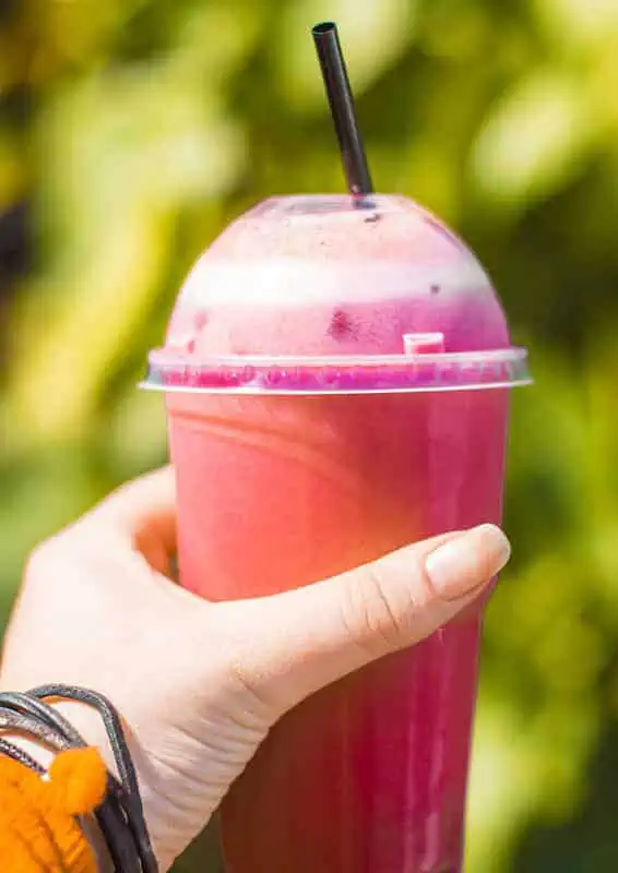 Where To Eat In Rarotonga: BEST Restaurants & Cafes 2025 8 A hand holding a vibrant pink smoothie from Punanga Nui Market, one of the best places to eat in Rarotonga for breakfast.